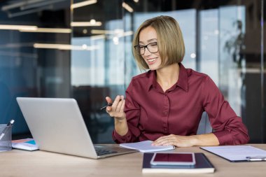 Genç Asyalı iş kadını video konferansı için dizüstü bilgisayar kullanıyor, uzaktan görüşme yapıyor, ya da modern bir şirket ofisinde çalışırken çevrimiçi bir webinara katılıyor.