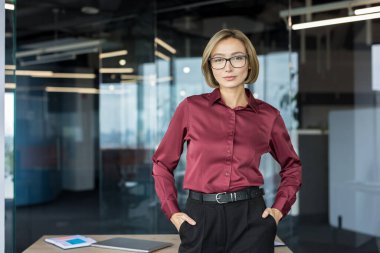 Çağdaş bir ofis ortamında duran profesyonel genç iş kadını, doğrudan geleceğe bakarken güven, liderlik, kararlılık ve başarı gösteriyor.