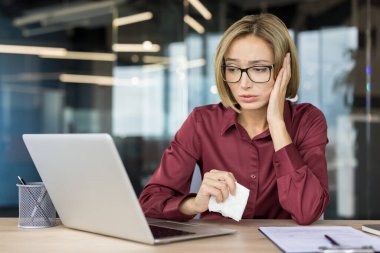 İş kadını üzgün ve bunalmış hissediyor. Ofiste dizüstü bilgisayarına bakarken elinde bir mendil tutuyor. Üzüntü, kötü haber ve tükenmişlik duygularını aktarıyor.