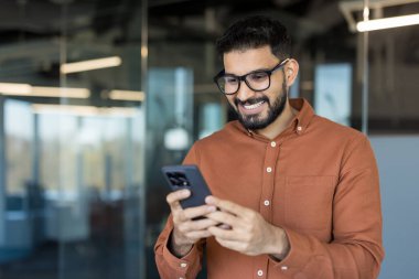 Cep telefonuyla mesajlaşırken gülümseyen gözlüklü genç, sakallı Hintli adam, bir şirket ofisinde arkadaşlarıyla ya da iş arkadaşlarıyla iletişim kurup eğleniyor.