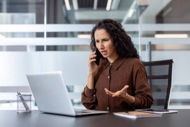 İş kadını, zor bir telefon görüşmesi sırasında hayal kırıklığı ve stres yaşıyor. Modern bir şirket ofisinde dizüstü bilgisayarla çalışırken, çatışma ve sorun çözme hissiyle iletişim kuruyor.