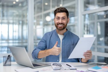 Parlak, modern bir ofiste gülümseyen sakallı bir işadamı elinde bir belge tutarak, mesleki güvenini, başarısını ve memnuniyetini gösteren bir belge veriyor.