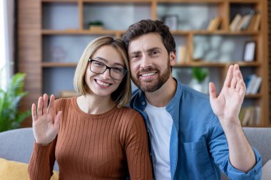 Video görüşmesi sırasında gülümseyen ve el sallayan mutlu çift, evden uzaktan iletişim kuruyor, bağlantı gösteriyor ve modern teknolojiyi iletişimde kalmak için kullanıyor.