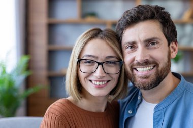 Mutlu genç çift, kameraya bakarak, ve geniş bir gülümseme, sevgi, ilişki ve beraberlik kavramları somutlaştırıcı modern ev ortamında