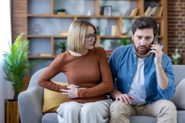 Kanepede şiddetli karın ağrısı çeken bir kadın endişeli kocası evde rahatsızlığı ve hastalığı için tıbbi yardım isterken acil bir telefon görüşmesi yapıyor.