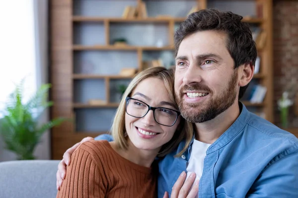 Mutlu çift kucaklaşması, sakallı bir adam ve gözlüklü bir kadın, evdeki kanepede oturuyor ve mutlu bir gülümsemeyle mutlu bir anı paylaşıyor.