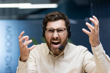 Ofiste kameranın önünde oturan ve ellerini sallarken öfkeyle konuşan öfkeli genç bir adamın portresi..