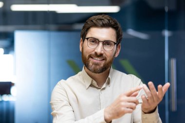 Ofiste kameranın önünde oturan, video görüşmesiyle konuşan, açıklama yapan ve parmaklarına güvenen genç bir adamın yakın plan portresi..