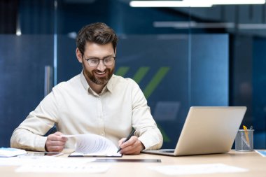 Belgeler ve raporlarla büroda çalışan gülümseyen genç işadamı.