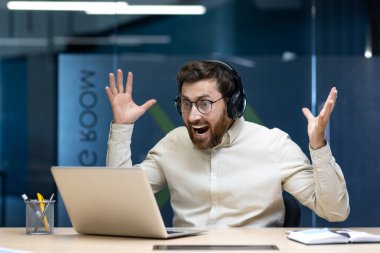 Kulaklıklı genç bir adamın ofis masasında oturup dizüstü bilgisayara hevesle bakması, ellerini kaldırması ve başarıyla sevinmesi hoş bir sürpriz oldu..