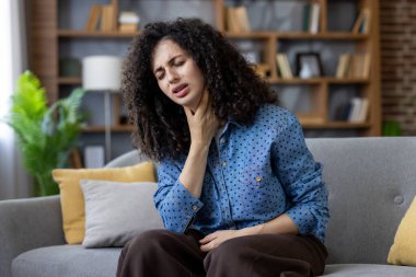 Kanepede boğazı ağrıyan genç bir kadın. Hasta ve bitkin görünüyor. Boğaz ağrısı, grip benzeri semptomlar ve genel olarak rahatsızlığı var.