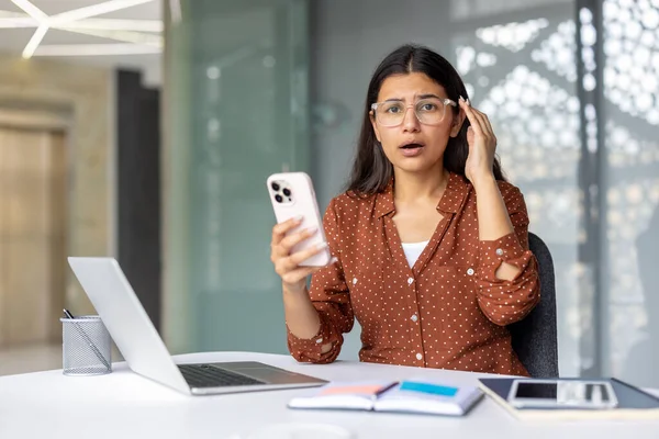 Ofis masasında çalışan genç Hintli kadın elinde akıllı bir telefon tutarken şok ve şaşkınlığını dile getiriyor ve beklenmedik kötü haberlere ya da sürpriz bir mesaja tepki veriyor.