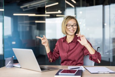 Mutlu iş kadını ofis masasında dans ederken sevinç duyuyor ve başarıyı kutluyor. Modern bir çalışma alanında başarılarını ve olumlu kariyer gelişimlerini ifade ediyor.