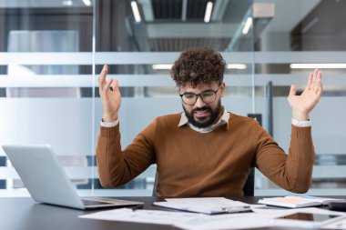 İşadamı hayal kırıklığına uğramış ve çileden çıkmış görünüyor. Ofis masasında dizüstü bilgisayar ve belgelerle otururken çaresizce el kaldırıyor. Bir sorunla uğraşıyor.