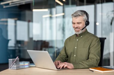 Müşteri desteği ve tele pazarlama hizmetleri sunan deneyimli bir adam, müşteri ve iş arkadaşlarıyla etkin bir şekilde iletişim kurarken aynı zamanda teknolojiyi uzaktan çalışma için kullanıyor.