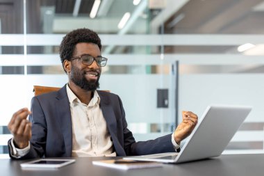 Genç işadamı, ofisteki masada otururken Lotus pozisyonunda meditasyon yapıyor. Adam dizüstü bilgisayarla online meditasyon kurslarına göz atıyor.