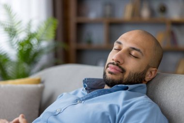 Genç adam rahat koltukta huzurlu bir uyku çekiyor, rahat ev ortamında sakin bir rahatlama ve stresin tadını çıkarıyor, gözlerini kapatıyor ve huzuru buluyor.