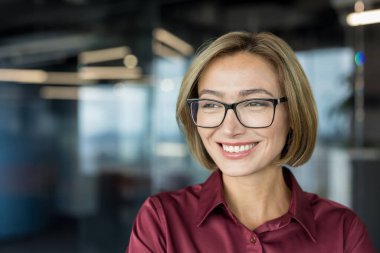 Kurumsal ofis ortamında genç profesyonel bir iş kadını, özgüvenle gülümseyen ve başka tarafa bakan, başarıyı, liderliği ve pozitif iş tutumunu temsil eden