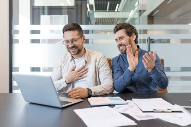 İki gülümseyen iş adamı, başarılı bir video görüşmesine veya modern bir ofis çalışma alanından online konferansa katılırken alkışlıyor ve minnettarlıklarını gösteriyorlar.