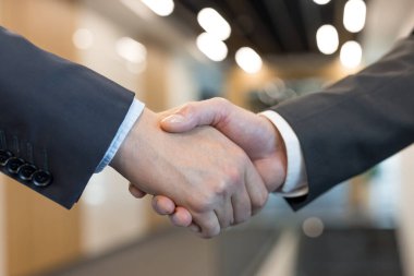 Koyu takım elbiseli iki iş adamı, anlaşmayı, ortaklığı, başarıyı, iş birliğini ve profesyonel bir şirkete olan güveni sembolize ediyor.