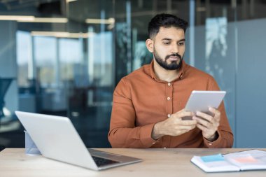 Genç Hintli işadamı, modern teknolojiyi günlük işler için kullanıyor ve çağdaş bir ofis ortamında kurumsal sorumlulukları yönetiyor.