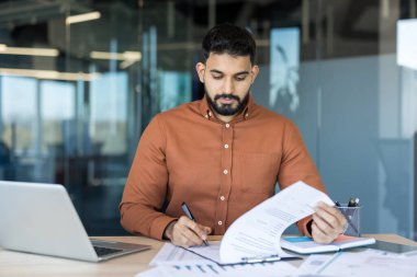 Modern bir ofis masasında çalışan Hintli bir işadamı, evrakları inceleyip imzalıyor, odaklanma ve profesyonellikle belgeleri yönetiyor, işletme yönetimi ve kurumsal iş akışını temsil ediyor.