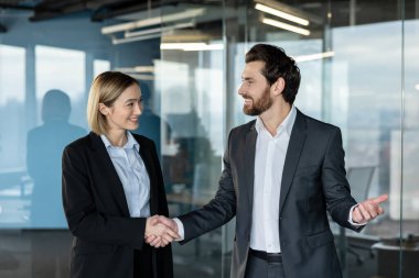 İki gülümseyen iş adamı modern bir ofiste el sıkışıyor başarılı bir ortaklığı, anlaşmayı, işbirliği ve kurumsal çevreye olan güveni simgeliyor.