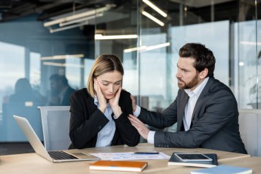 İş adamı, ofis masasındaki kadın meslektaşını sinirlendiriyor. Yorgunluk, stres ve işyeri yorgunluğuyla başa çıkarken empati ve duygusal destek sunuyor.