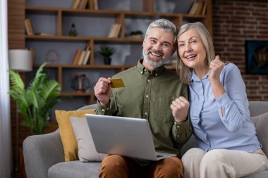 Üst düzey çiftler dizüstü bilgisayarda başarılı satın alımları kutluyorlar. Kredi kartı tutan adam, karısını yumruklayan adam, eski nesillerin e-ticaret, bankacılık ve dijital yaşam tarzını temsil eden kişi.