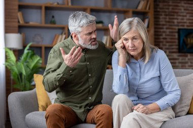 Olgun bir adam, üzgün karısına yüksek sesle el kol hareketi yapıyor ve bağırıyor. O da koltukta oturuyor ve aşağıya bakıyor. İlişkilerindeki sorunlar yüzünden üzgün ve üzgün hissediyor.