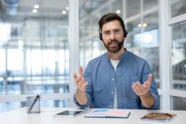 Arkadaşça bir video görüşmesi sırasında konuşan ve hareket eden adam, müşteri desteğini, uzaktan yardımı, sanal iletişimi ve ofis çalışma alanından profesyonel yardımı sembolize ediyor.