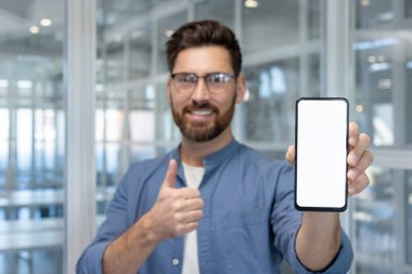 Uygulama gösterimi ya da mesajlaşma kavramları için başparmak hareketi yaparken boş beyaz ekranlı akıllı telefonu elinde tutan olumlu bir adam.