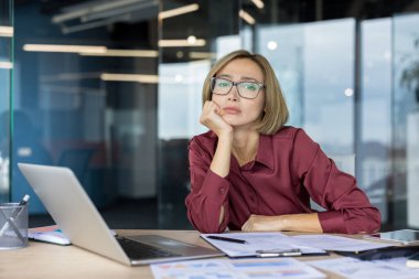 Ofis masasındaki iş kadını elinde laptop ve kağıtlarla son teslim tarihlerinden, baskıdan ve aşırı çalışmaktan bitkin düşmüş ve bunalmış bir halde.
