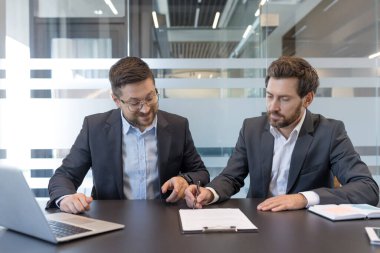 İki profesyonel işadamı, bir şirket toplantısında, modern ofis ortamında bir ortaklık anlaşmasını sonuçlandırmak için bir panoya yasal bir belge imzalayıp işbirliği yapıyorlar.