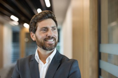 Profesyonel işadamı başka tarafa bakıyor, modern bir ofiste özgüvenle gülümsüyor, başarıyı, kariyer başarısını, şirket liderliğini ve geleceğe olumlu bir bakış açısını temsil ediyor.