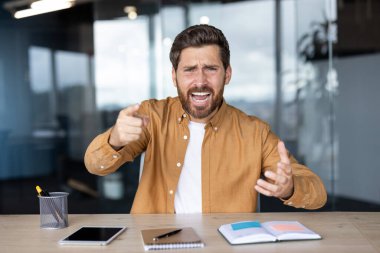 Sinirli bir çalışan iş yerinde stres ve çatışma içindedir. Öfke ve saldırganlık duygularını ifade ederken, bir yandan da doğrudan izleyiciyi işaret eder.