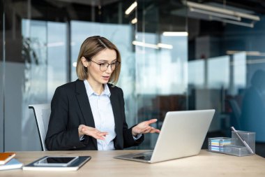 İş kadını, modern bir ofisten bilgisayarına yaptığı video mesajı sırasında sanal bir toplantı yönetirken ve uzaktan iş arkadaşlarıyla işbirliği yaparken fikirlerini anlatıyor.
