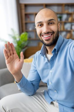 Sakallı genç ve kel bir adam video görüşmesi ya da internet görüşmesi sırasında kameraya gülümsüyor ve el sallıyor. Evden iletişim, uzaktan çalışma ve bağlantı kavramları yaratıyor.