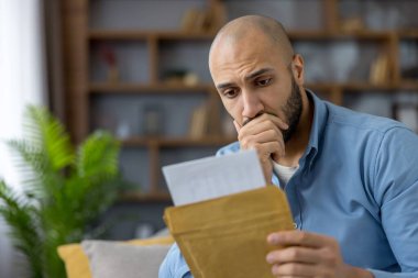 Huzursuz bir adam, oturma odasında otururken elinde kahverengi bir zarf ve kağıtlar tutan bir mektuptan kötü beklenmedik bir haber ya da şok bildirisi alır.