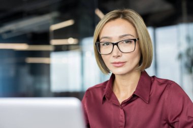 Bilgisayarda çalışırken kameraya bakan kendine güvenen profesyonel iş kadını, başarıyı, liderliği ve çağdaş ofis ortamında modern bir şirket kariyerini temsil ediyor.