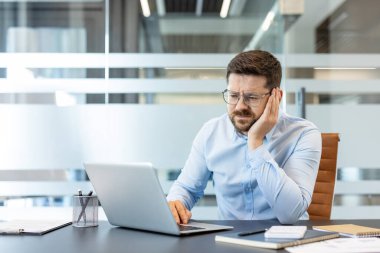 İş adamı hayal kırıklığını ve hayal kırıklığını ifade ediyor. Ofis masasında dizüstü bilgisayar üzerinde çalışırken baş ağrısı çekiyor. Profesyonel stresle uğraşıyor.