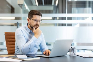 Günümüz ofis ortamında dizüstü bilgisayarında işine yoğunlaşan düşünceli işadamı, yeni fikirleri ve iş stratejisini yansıtıyor.