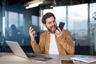 Modern bir ofisteki stresli işadamı cep telefonu tutarken duygusal patlamalar yaşıyor, çevrimiçi bir soruna kızgınlığını ve kızgınlığını dile getiriyor ya da iş sırasında zorlu bir telefon görüşmesi yapıyor.