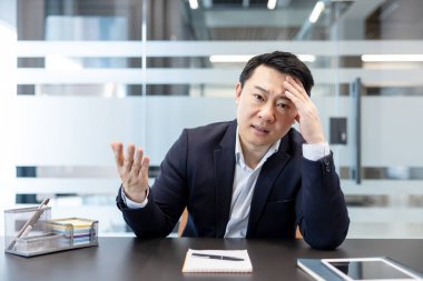 Asyalı işadamı, modern ofis ortamında ağır iş yükü ve şirket baskısı yüzünden hayal kırıklığı ve tükenmişlik yaşıyor.