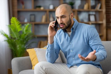 Evdeki bir kanepede rahat bir şekilde oturan genç adam ciddi bir telefon görüşmesi yapıyor. Yüzündeki ifade ve el hareketleriyle endişelerini dile getiriyor.