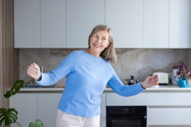 Emekliliğin tadını çıkaran yaşlı bir kadın, çağdaş mutfağında mutlu, zinde ve sağlıklı bir yaşam tarzını ifade ederek mutlu ve mutlu bir şekilde gülümsüyor.