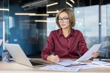 Özgüvenli iş kadını özenle çalışıyor, evrak işlerini organize ediyor ve masasında modern bir çalışma alanında anlaşmalar imzalıyor, profesyonel rolüne odaklandığını ve uzmanlığını gösteriyor.