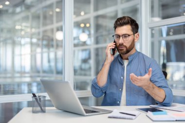 Akıllı telefondan iletişim kuran, yaratıcı ofiste masa başında oturan, önemli projeleri tartışan ya da odaklanmış bir ifadeyle iş kararlarını veren genç bir adam.