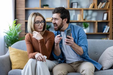 Evdeki hararetli bir tartışma sırasında elinde cep telefonu olan, çatışmayı, ihaneti ve kıskançlığı temsil eden bir adam üzgün bir kadına bağırıyor.