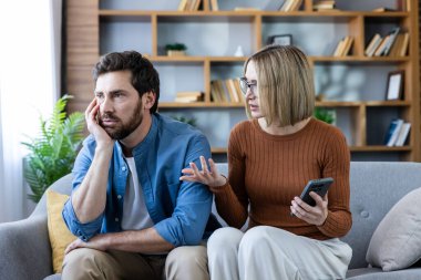 Üzgün bir adam ve duygusal bir kadın evde bir evlilik anlaşmazlığı yaşıyorlar, cep telefonu tutarken ilişkilerindeki sorunlar hakkında konuşuyorlar.